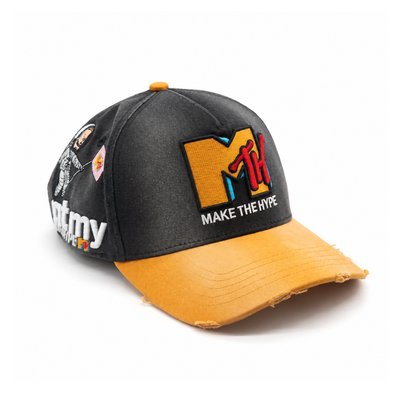 Quarter view of MAKE THE HYPE TV showing washed charcoal cotton, MTH embroidery, astronaut side detail and a lightly distressed golden-yellow brim